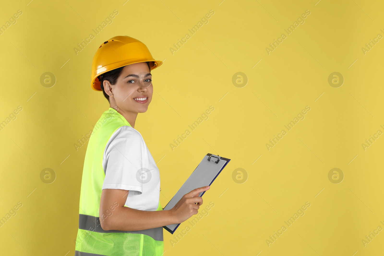 Photo of Engineer in hard hat with clipboard on yellow background, space for text