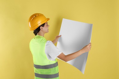 Engineer in hard hat with draft on yellow background