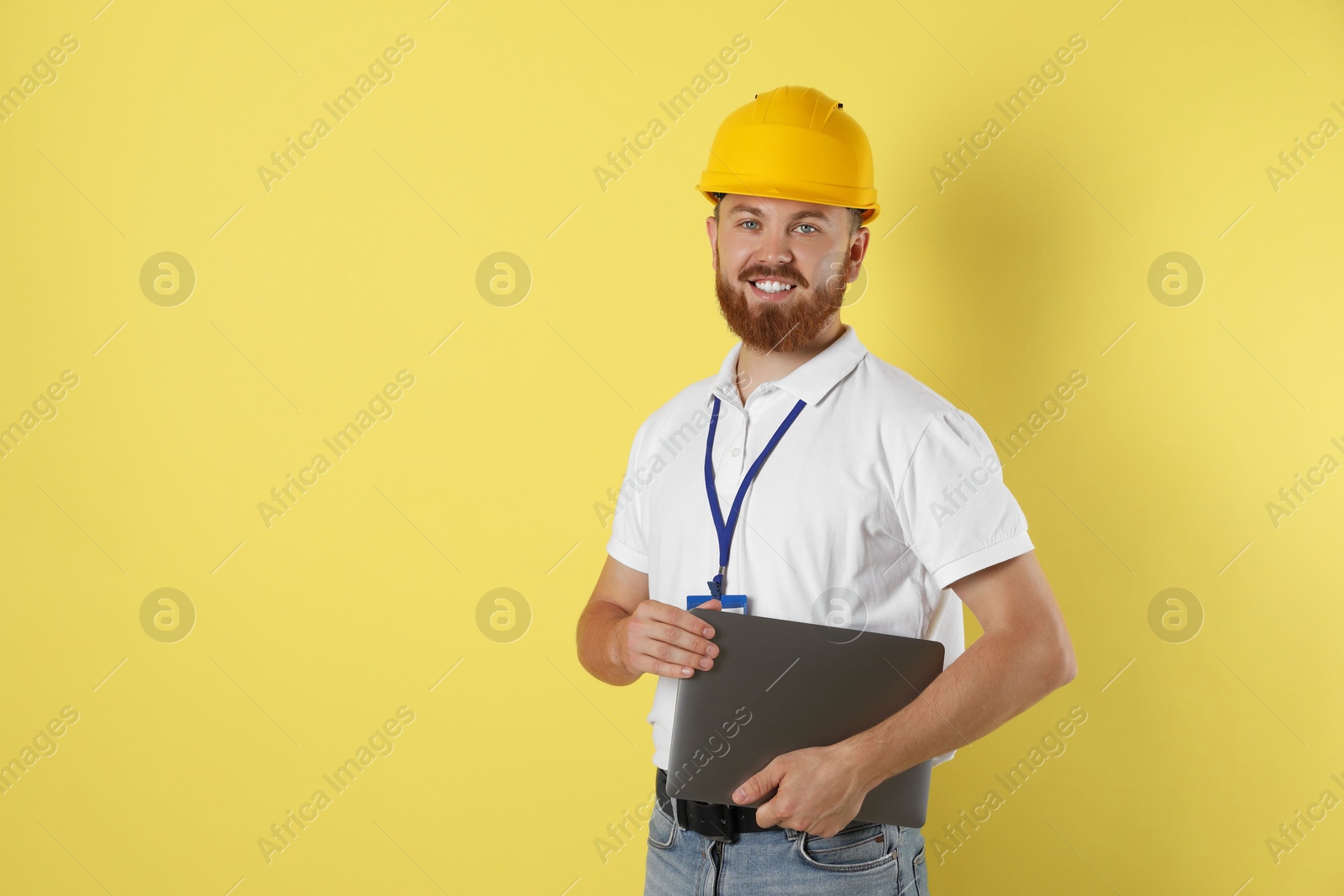 Photo of Engineer in hard hat with laptop on yellow background, space for text