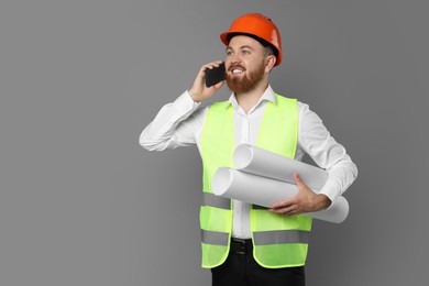 Engineer in hard hat with drafts talking on smartphone against grey background, space for text