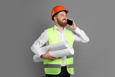Photo of Engineer in hard hat with drafts talking on smartphone against grey background