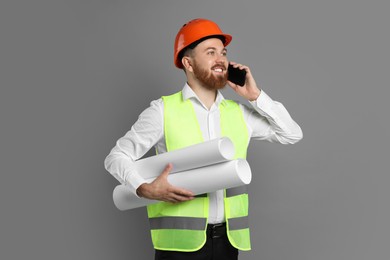 Engineer in hard hat with drafts talking on smartphone against grey background