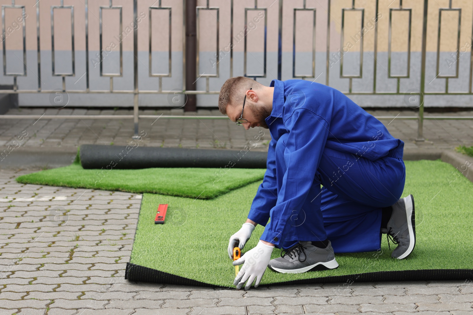 Photo of Young man in uniform installing artificial turf outdoors