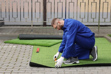 Young man in uniform installing artificial turf outdoors