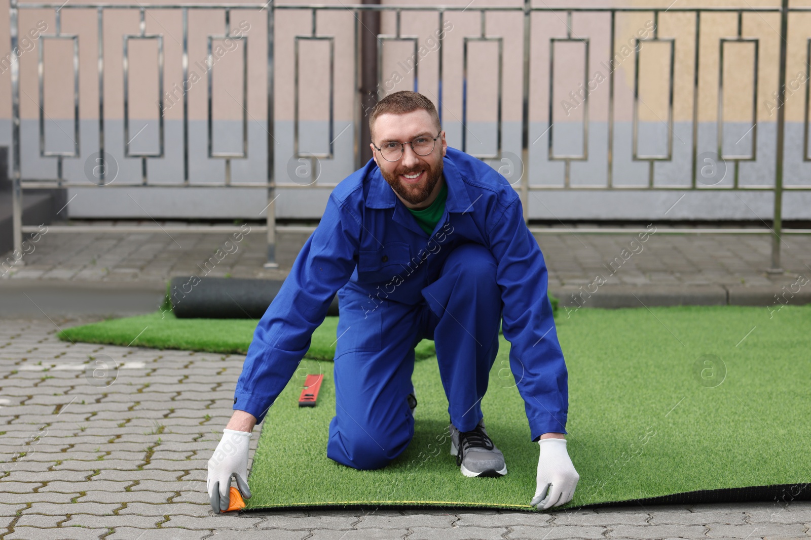 Photo of Happy young man installing artificial turf outdoors