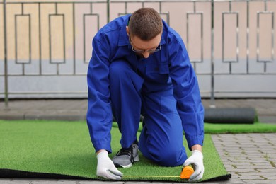 Photo of Young man in uniform installing artificial turf outdoors