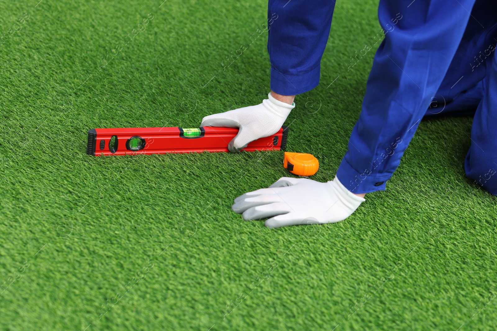 Photo of Man in uniform installing artificial turf, closeup