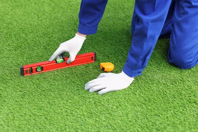 Photo of Man in uniform installing artificial turf, closeup