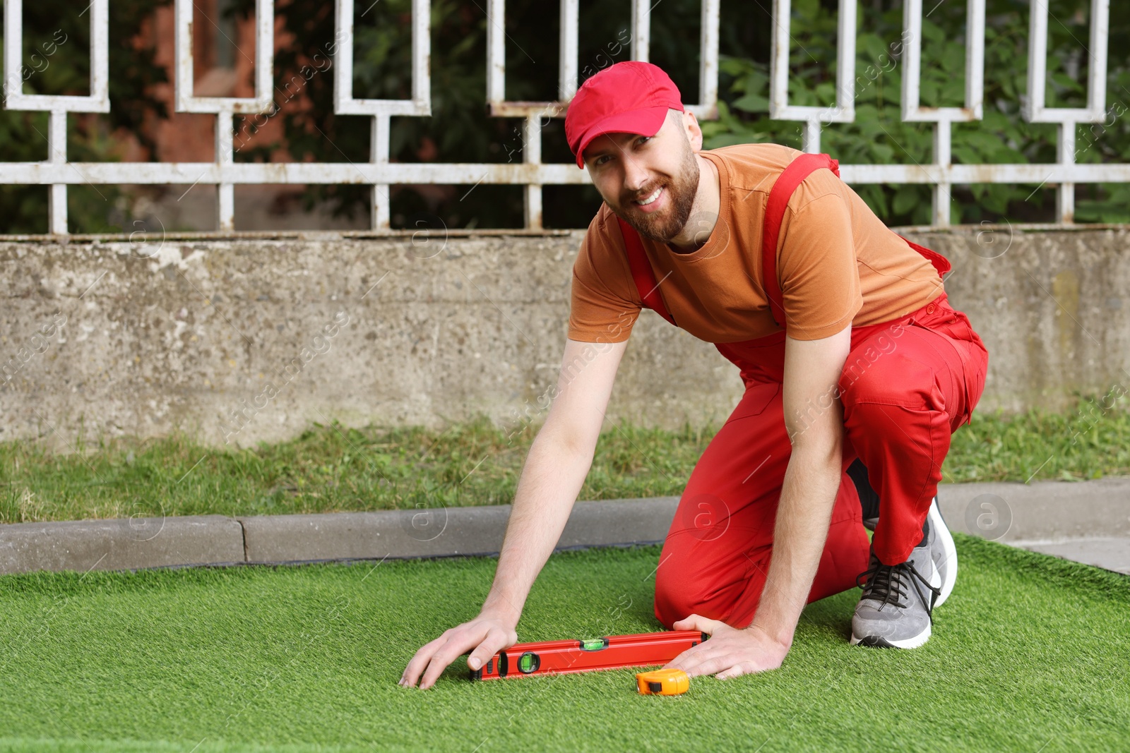 Photo of Happy young man installing artificial turf outdoors