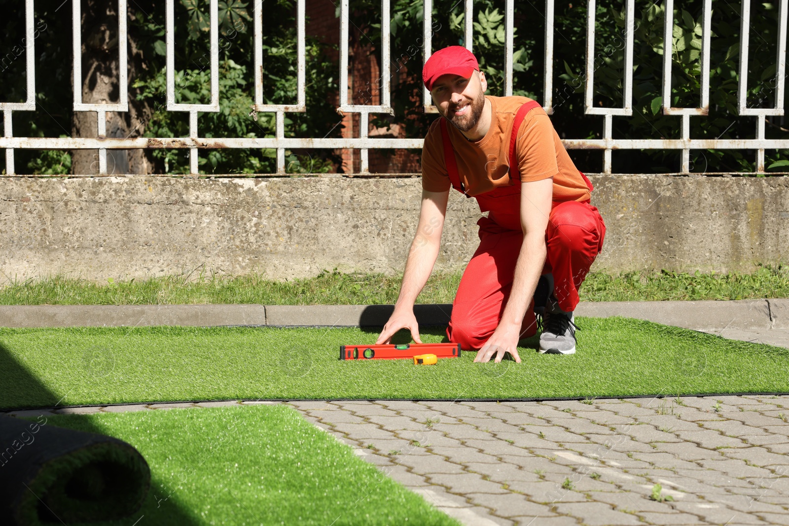 Photo of Happy young man installing artificial turf outdoors