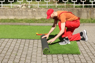 Photo of Young man in uniform installing artificial turf outdoors