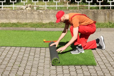 Young man in uniform installing artificial turf outdoors