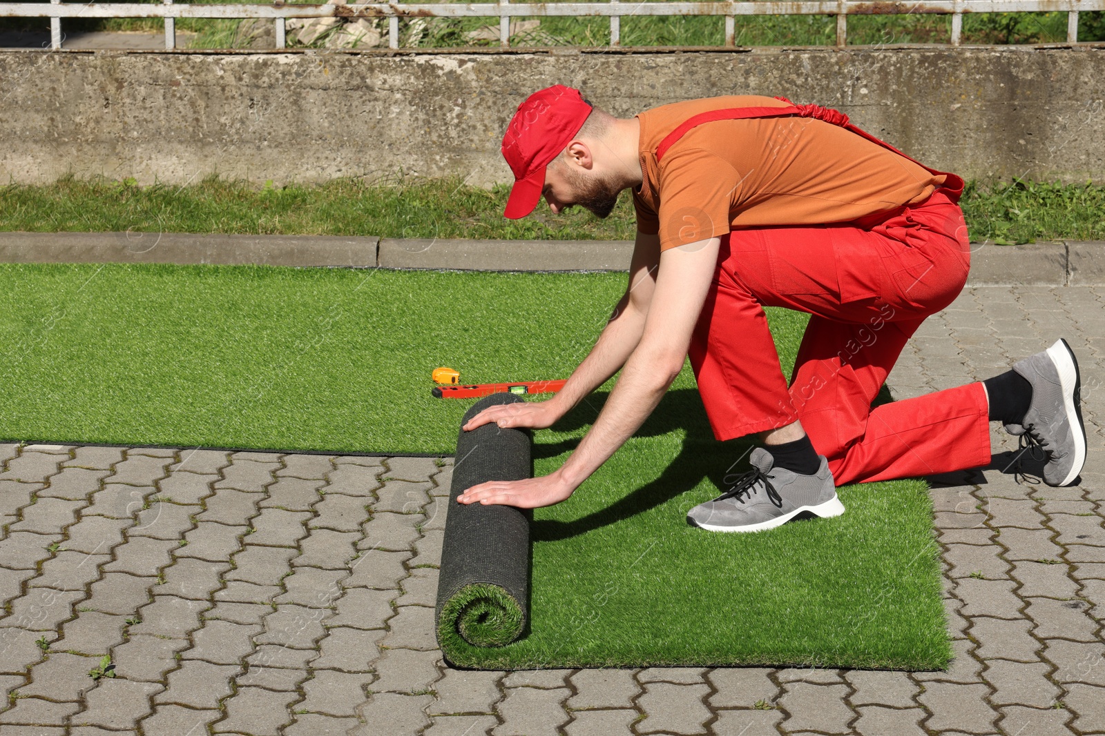 Photo of Young man in uniform installing artificial turf outdoors