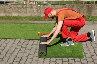 Young man in uniform installing artificial turf outdoors