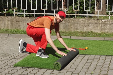 Photo of Happy young man installing artificial turf outdoors