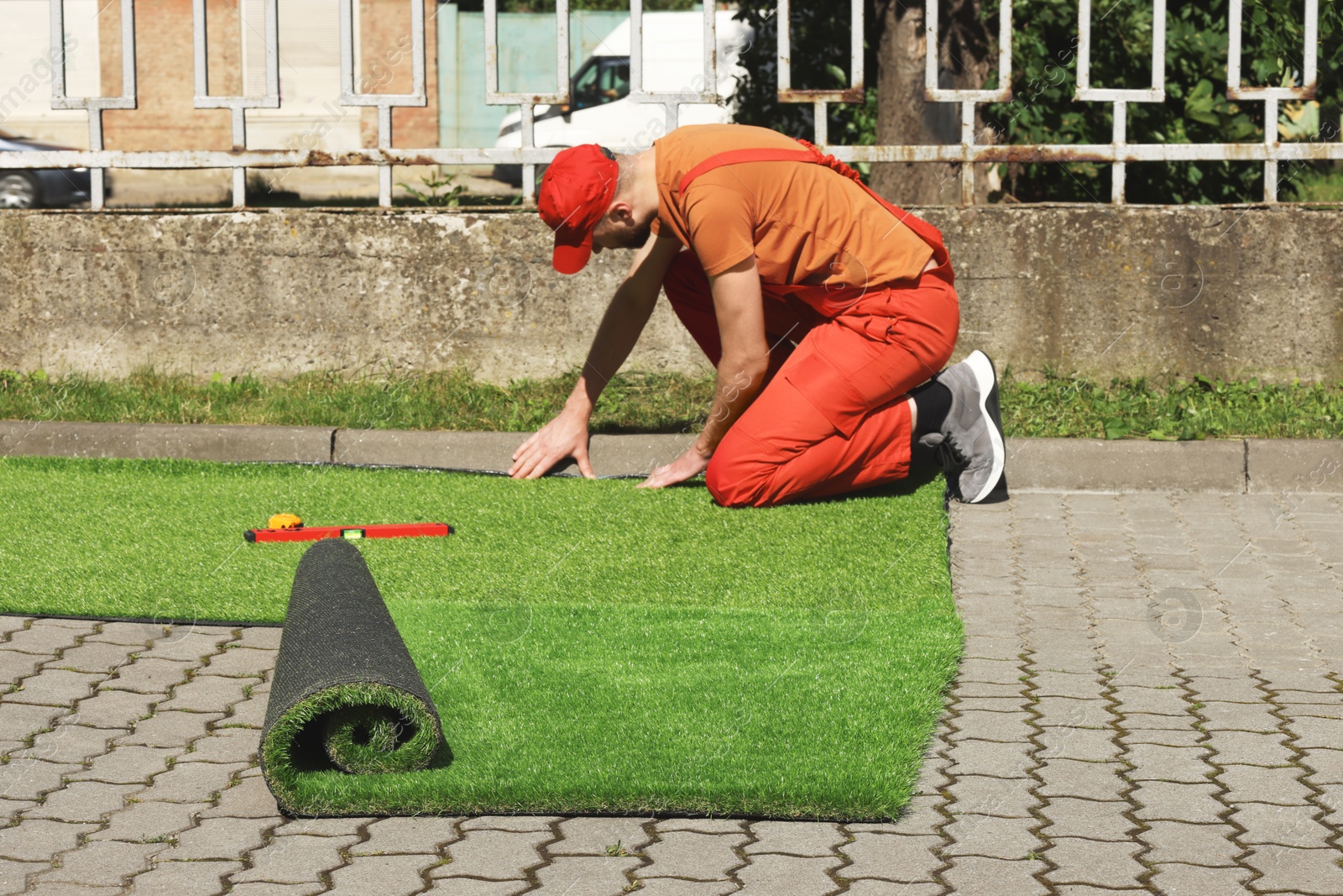 Photo of Young man in uniform installing artificial turf outdoors