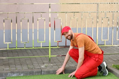 Photo of Happy young man in uniform installing artificial turf outdoors