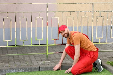 Happy young man in uniform installing artificial turf outdoors