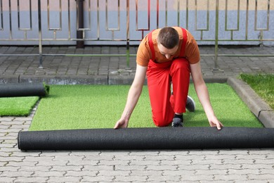 Photo of Happy young man installing artificial turf outdoors