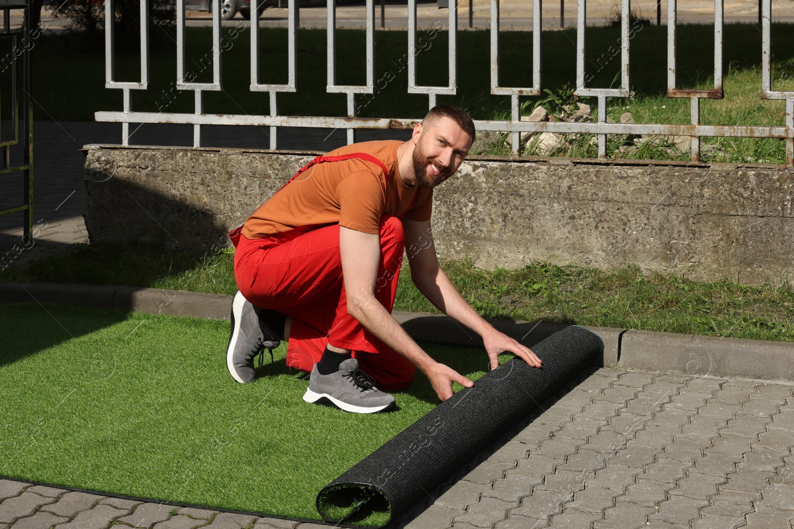 Photo of Happy young man in uniform installing artificial turf outdoors