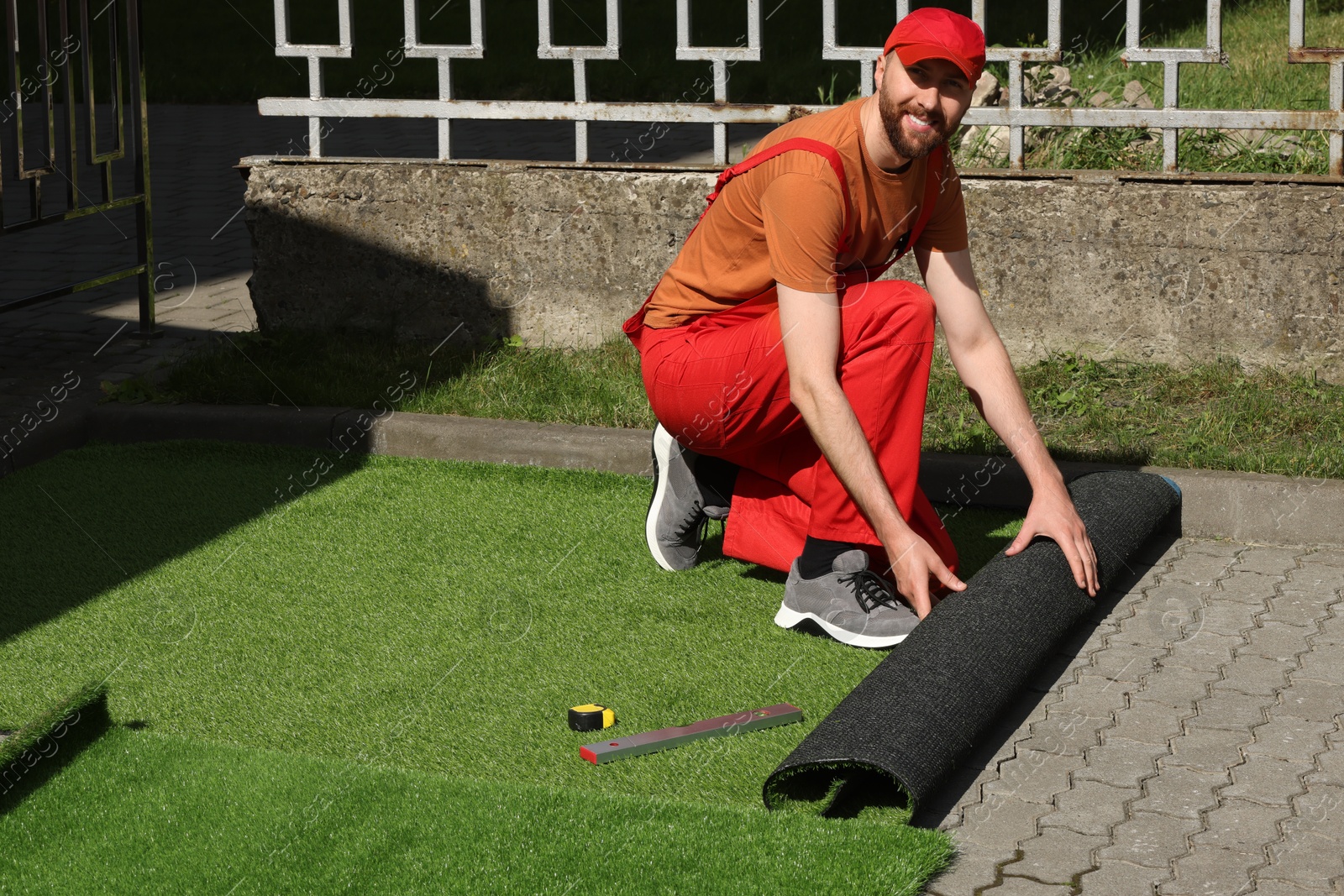 Photo of Happy young man in uniform installing artificial turf outdoors