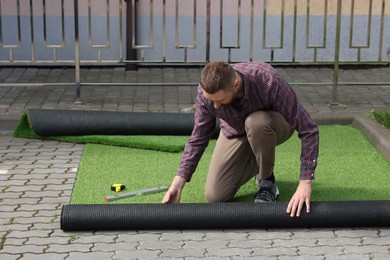 Photo of Young man installing artificial green turf outdoors