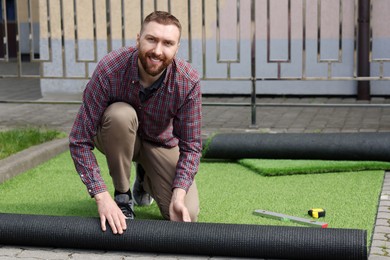 Photo of Happy young man installing artificial turf outdoors