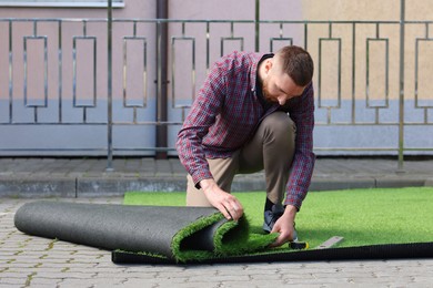 Young man installing artificial green turf outdoors