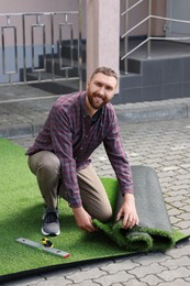 Photo of Happy young man installing artificial turf outdoors