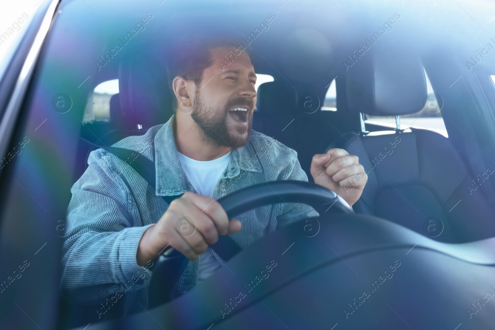 Photo of Man singing in car, view through windshield