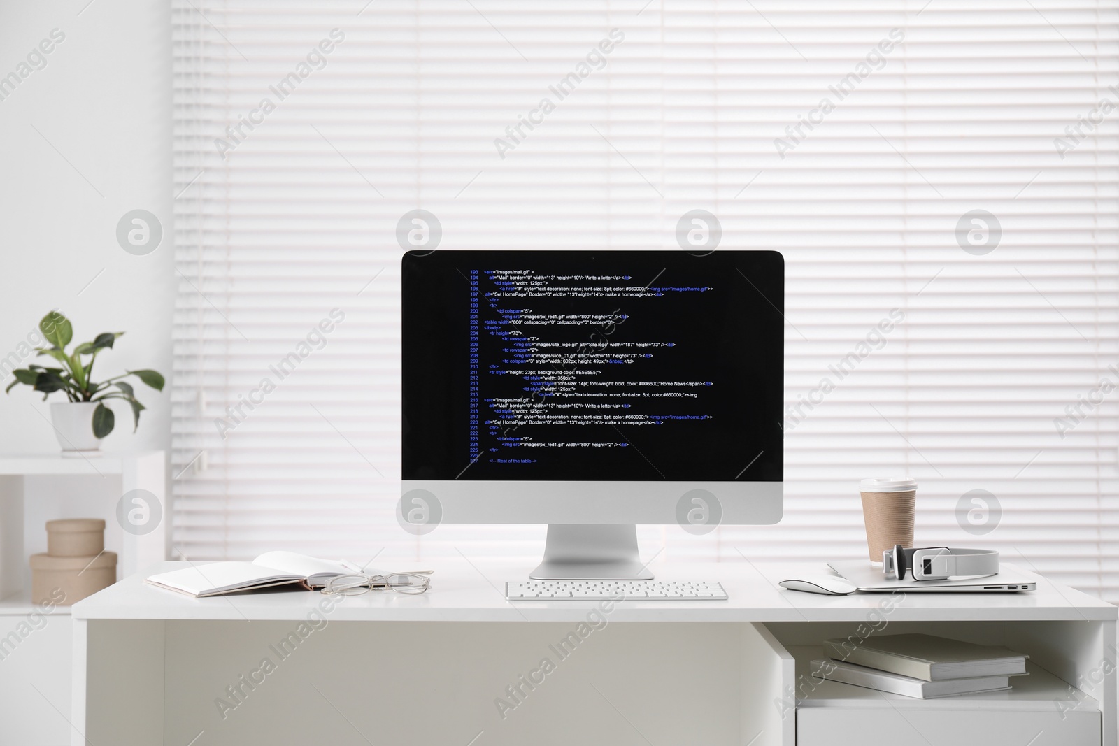 Photo of Programmer's workplace. Modern computer with unfinished code, coffee and supplies on desk