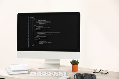 Photo of Programmer's workplace. Modern computer with unfinished code, headphones and supplies on desk