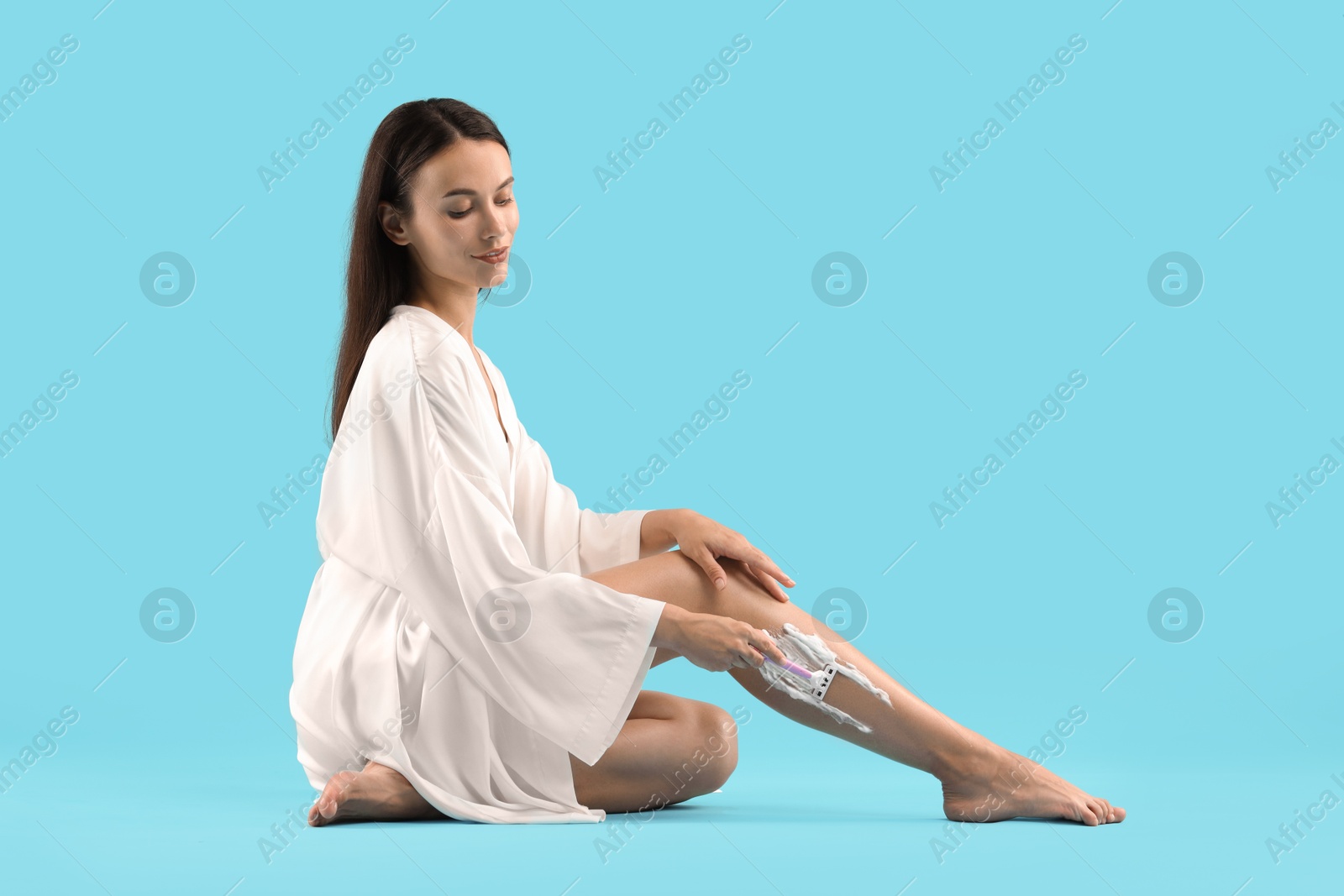 Photo of Beautiful woman shaving leg on light blue background