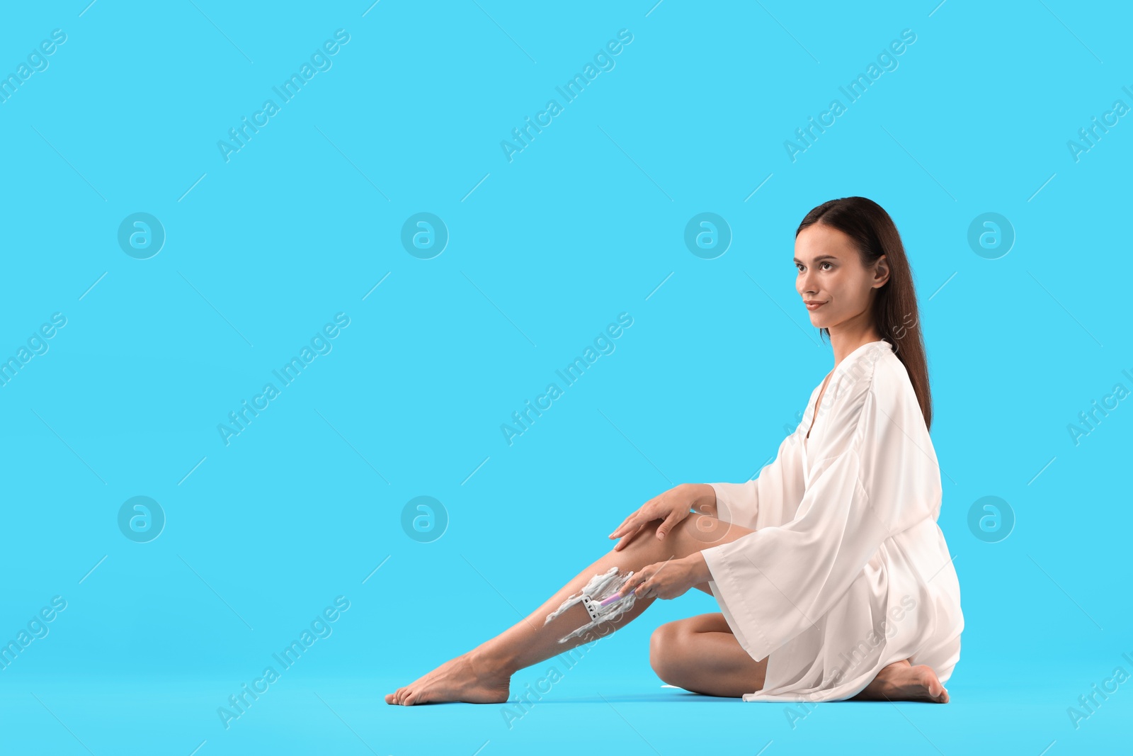 Photo of Beautiful woman shaving leg on light blue background. Space for text