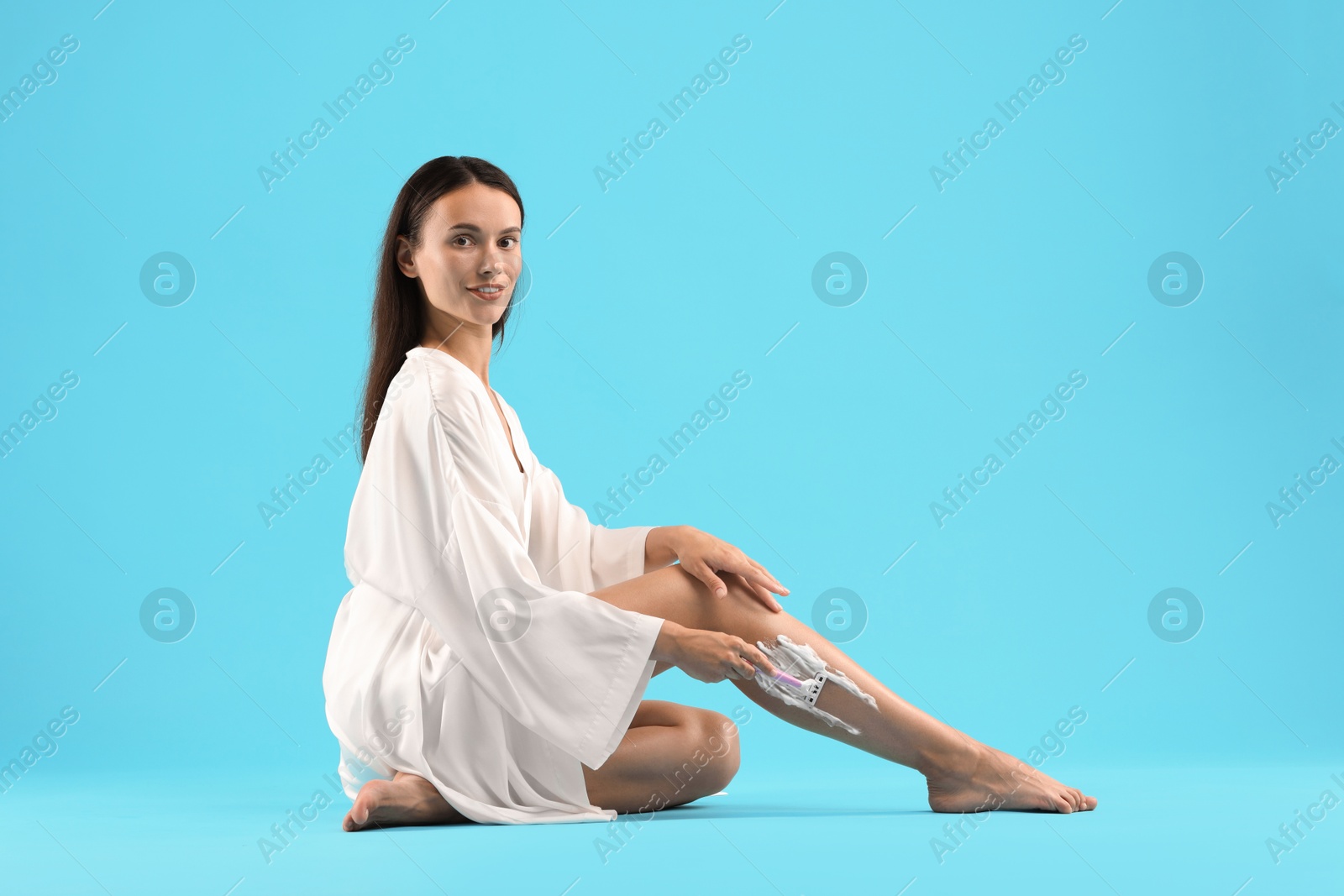 Photo of Beautiful woman shaving leg on light blue background