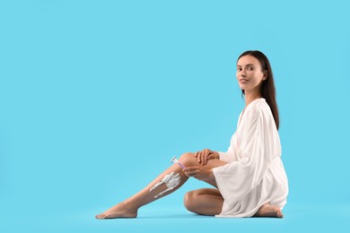 Smiling woman shaving leg on light blue background. Space for text