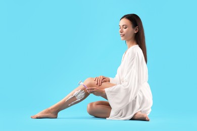 Smiling woman shaving leg on light blue background