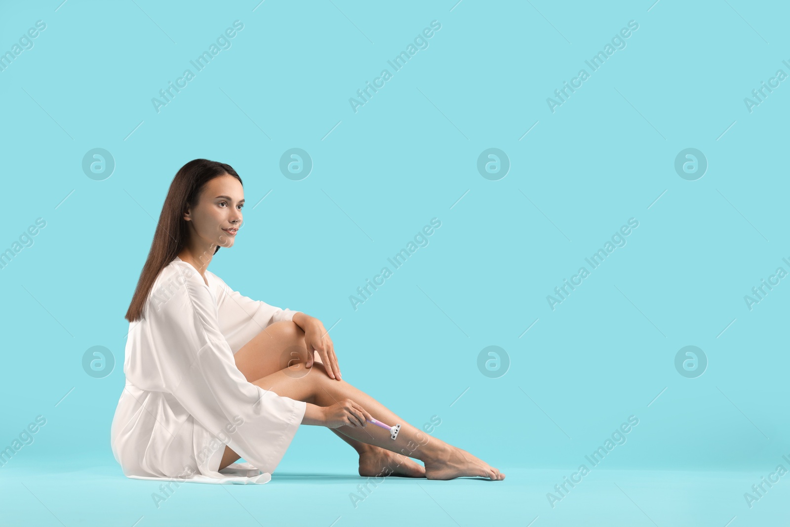 Photo of Beautiful woman shaving leg on light blue background. Space for text