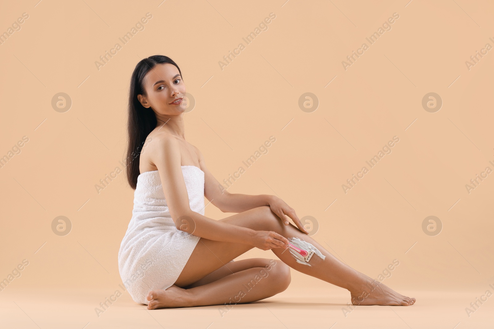 Photo of Smiling woman shaving leg on beige background