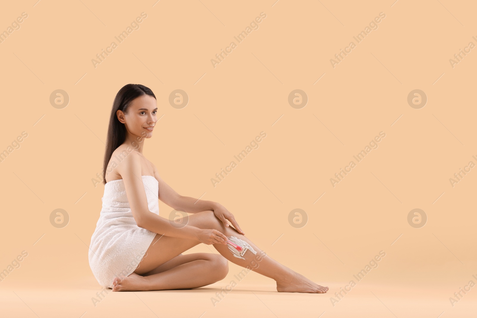 Photo of Smiling woman shaving leg on beige background. Space for text