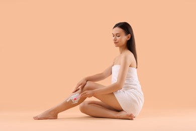 Beautiful woman shaving leg on beige background