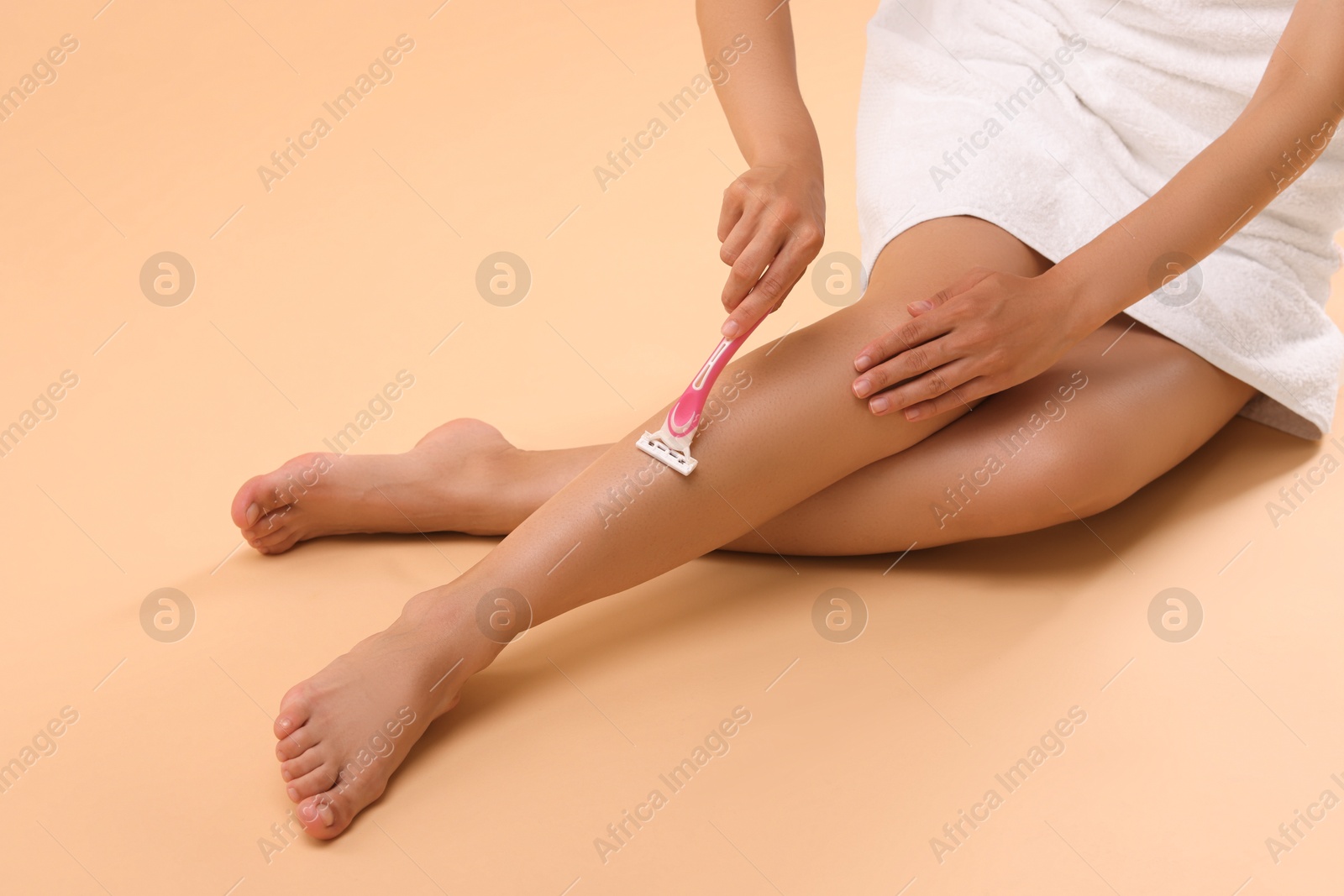 Photo of Woman shaving leg on beige background, closeup