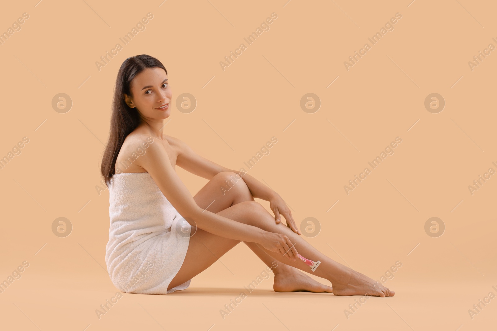 Photo of Smiling woman shaving leg on beige background