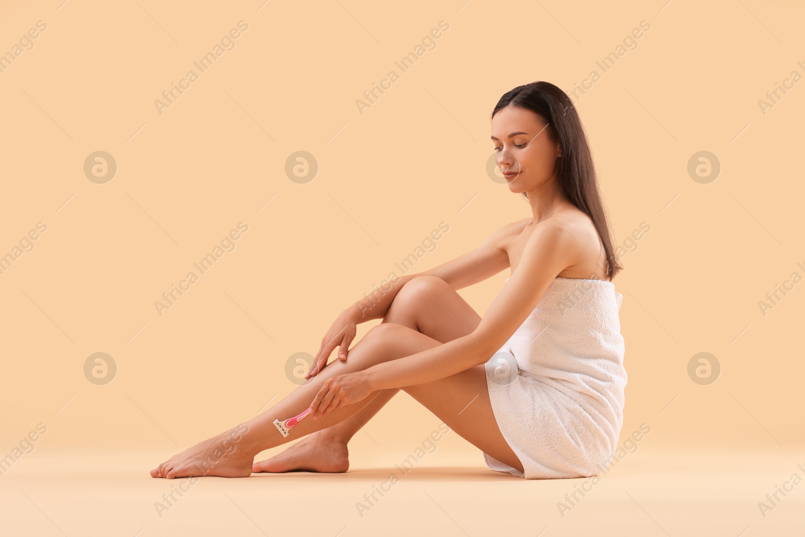 Photo of Beautiful woman shaving leg on beige background