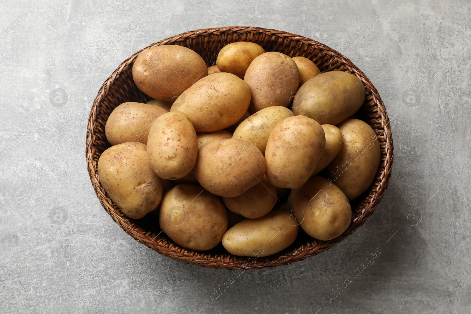 Photo of Many fresh potatoes in wicker basket on grey table, top view