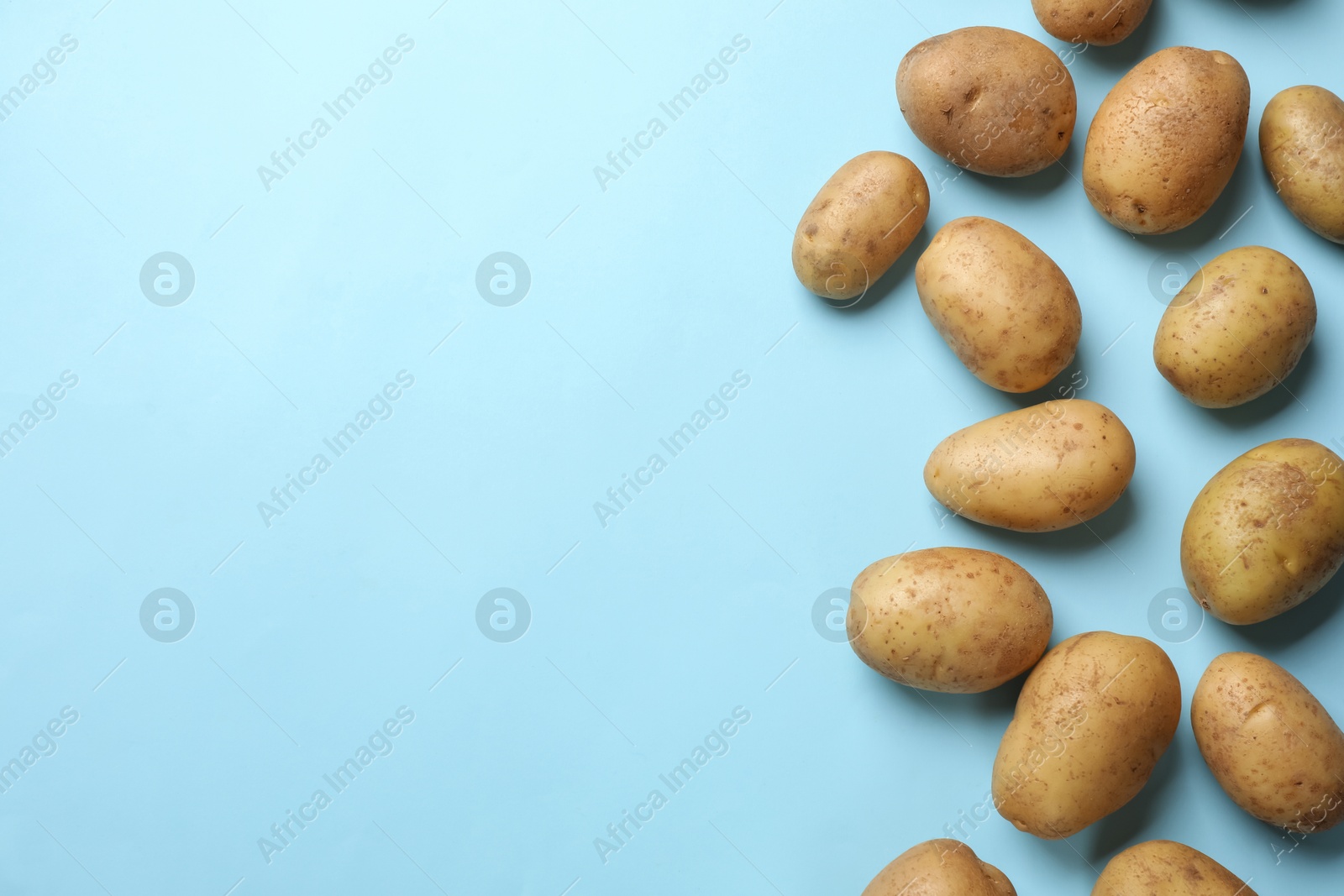 Photo of Many fresh potatoes on light blue background, flat lay. Space for text