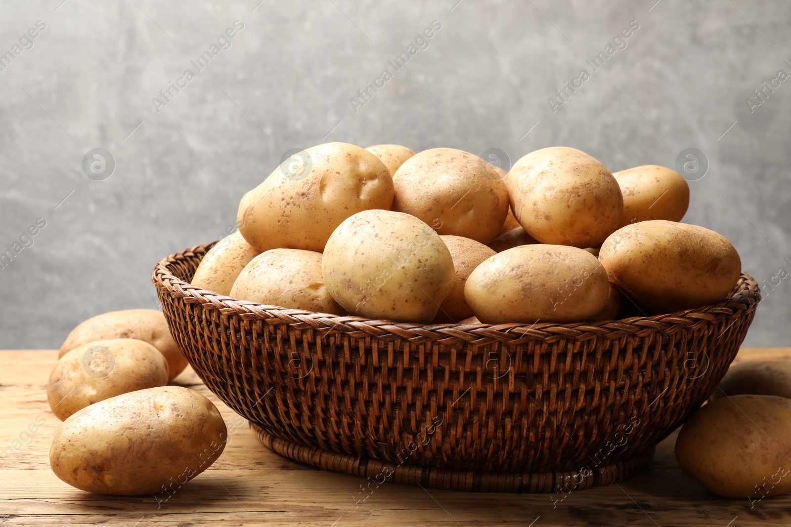 Photo of Many fresh potatoes in wicker basket on wooden table, closeup