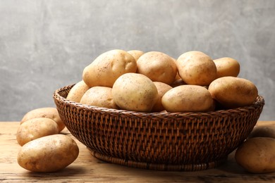 Photo of Many fresh potatoes in wicker basket on wooden table, closeup