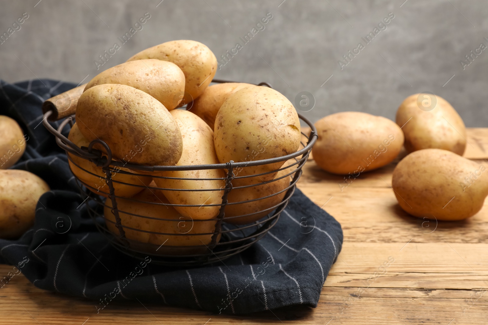 Photo of Many fresh potatoes in metal basket on wooden table, closeup