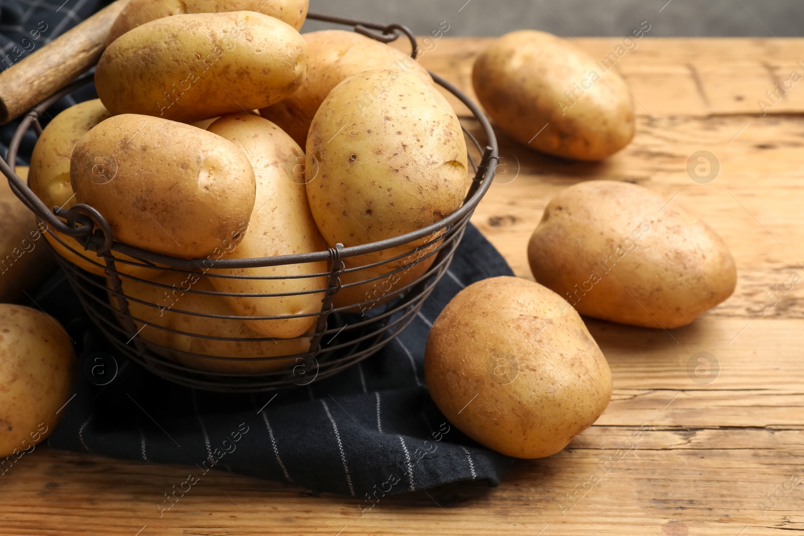 Photo of Many fresh potatoes in metal basket on wooden table, closeup